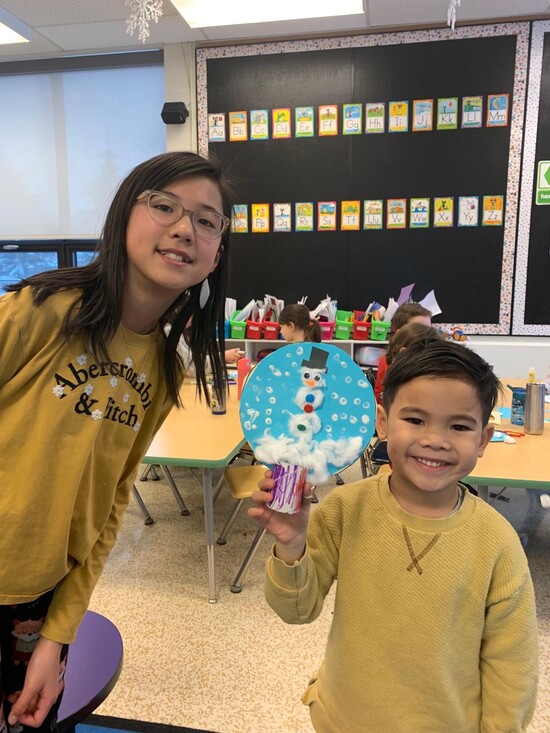 Kindergarten student showing his artwork with his Grade 6 cross-age buddy